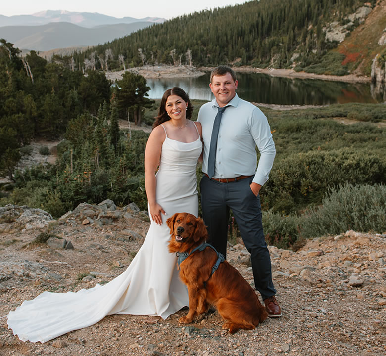 Newlyweds with their golden retriever in a harness beside an alpine lake in the Colorado mountains